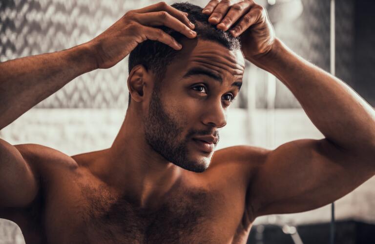 Young African American man checking hair and scalp in bathroom mirror