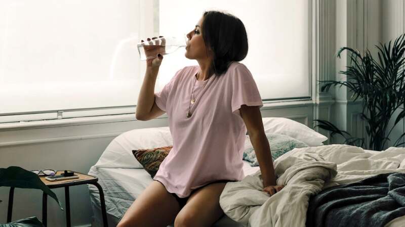 Woman drinking water on side of bed after waking up