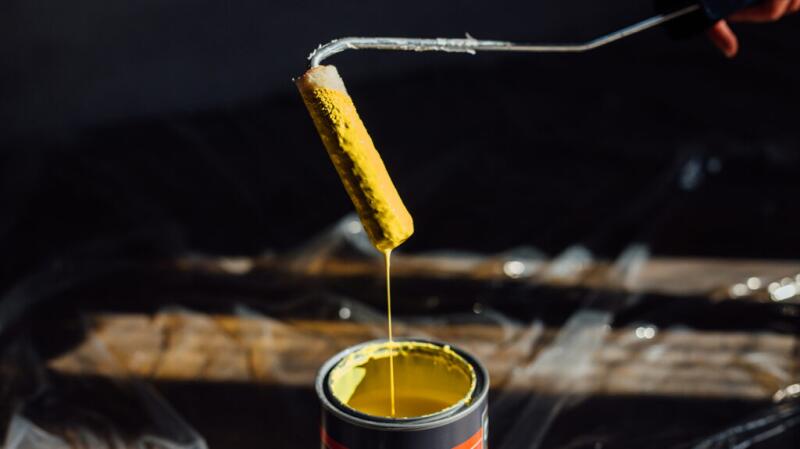 A paint roller dipping into a can of bright yellow paint