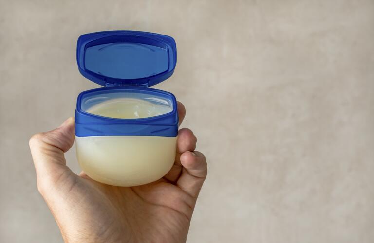 hand of a male person holds a container with Vaseline or petroleum jelly