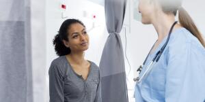 Young Hispanic female patient on exam table smiling at young Caucasian female doctor