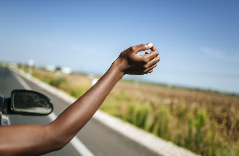 arm reaching out of passenger car window while driving on highway