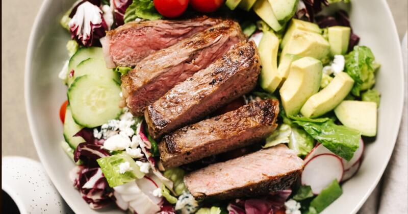 Cut pieces of steak sit on top of a green salad.
