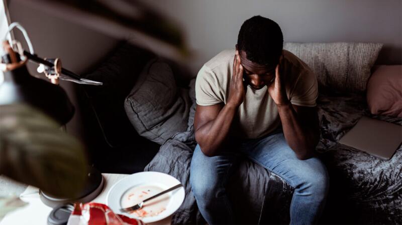 Male sitting on bed with his hands on his head, looking distressed or worried