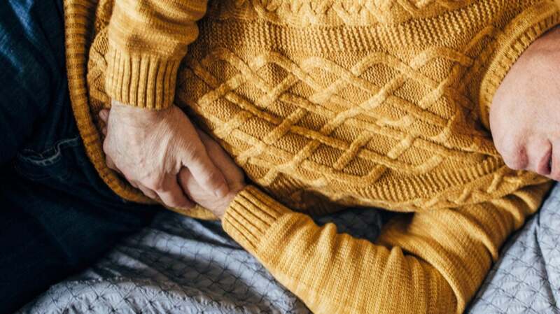 Closeup of a person with their hands over their stomach.