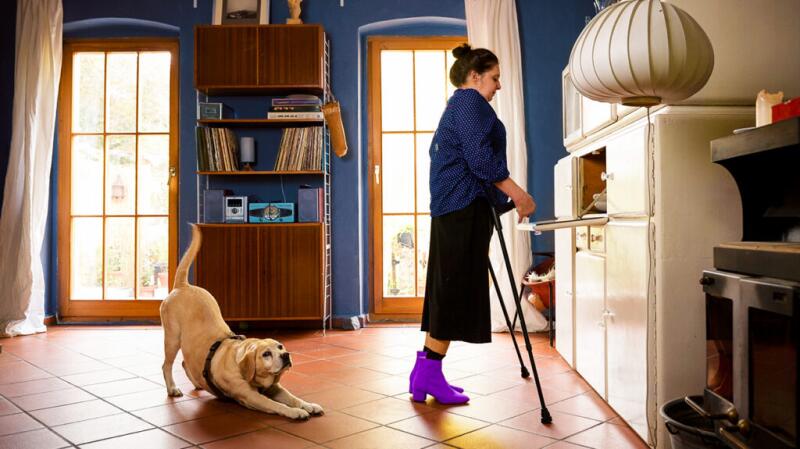 Woman stands with crutches with support dog by the side.