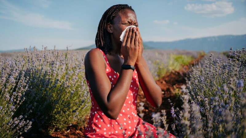 A woman sitting in a field of flowers and blowing her nose
