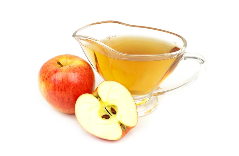apple cider vinegar in clear cup next to cut apple