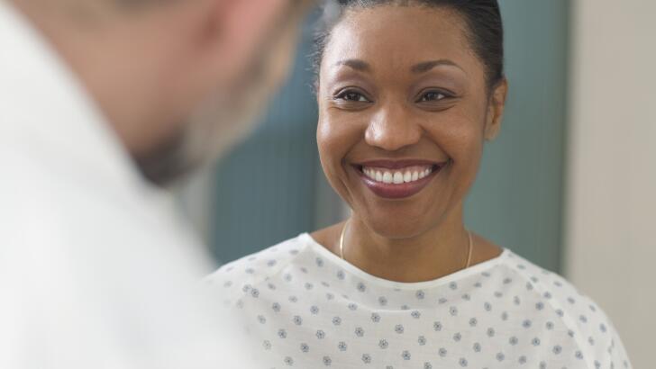 Close-up of African American female patient in hospital gown smiling at doctor