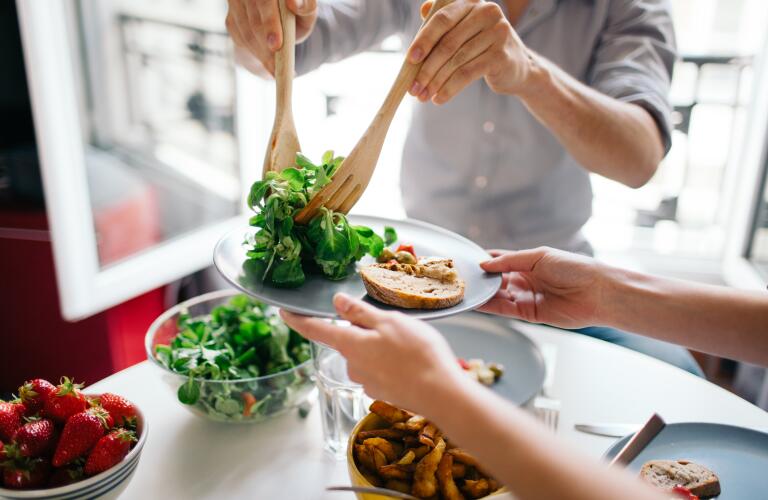 Cropped image of man serving salad to woman holding plate