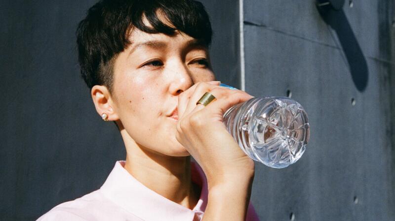 A person holds a clear plastic water bottle up to their lips to take a sip.