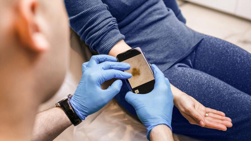 Doctor checking a person's skin and taking a picture of a spot