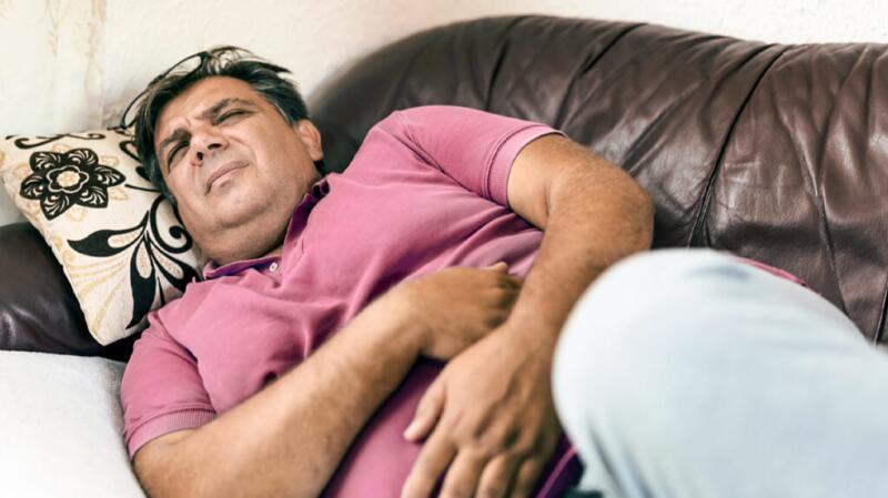 male feeling stomach pain at home as he lies on couch