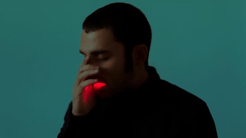 Photo illustration of darkly lit man holding hand over mouth with red light emitting from mouth