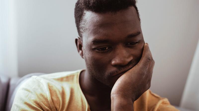 Close-up of man sitting with head in hand looking worried and staring straight ahead