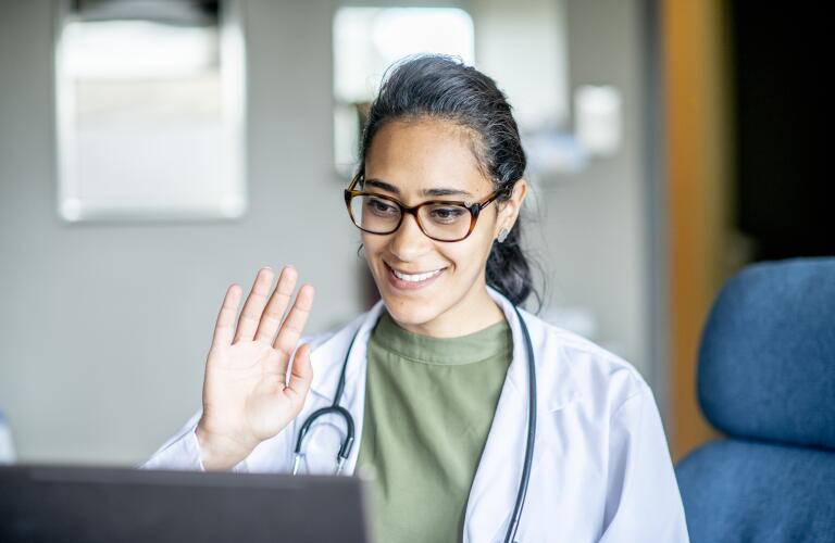 portrait of female doctor waving at computer screen during telehealth appointment