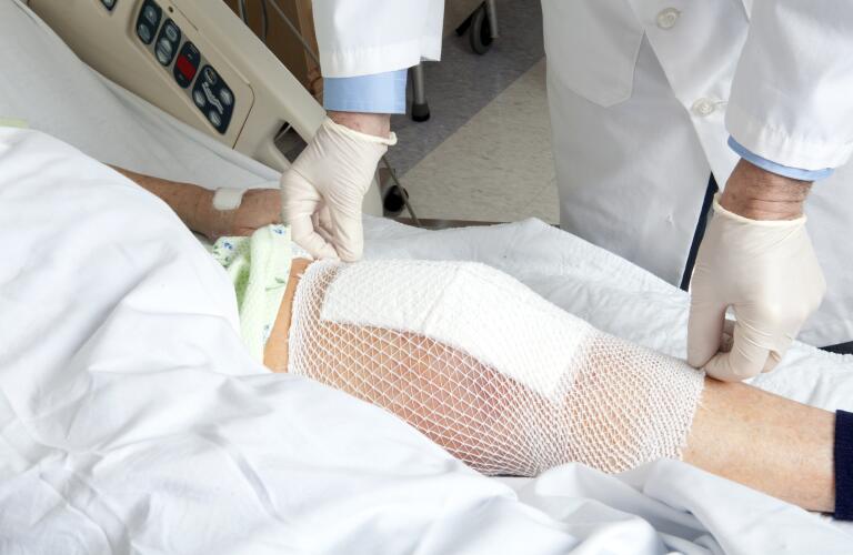 Unseen patient in hospital bed with knee replacement bandage