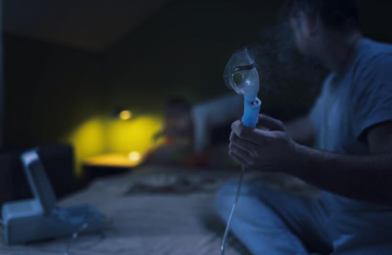 Man holding asthma nebulizer on bed at night