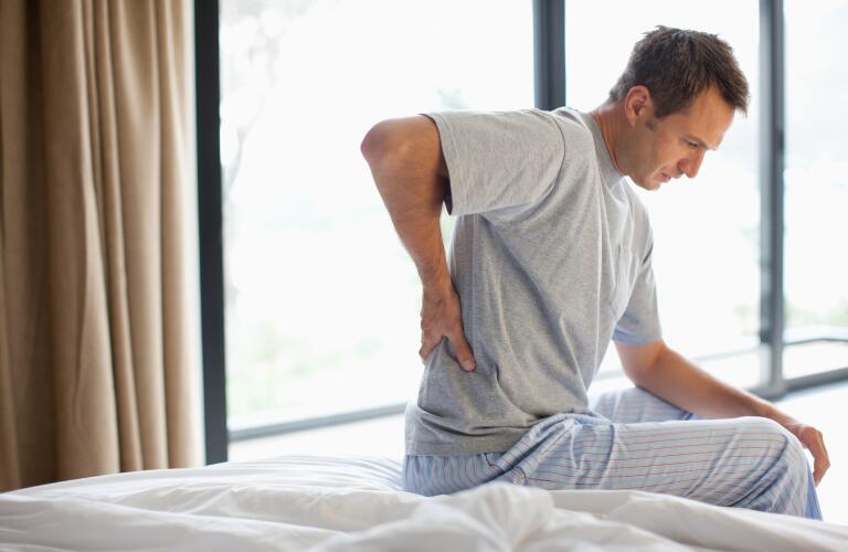 man-sitting-on-bed-holding-lower-back