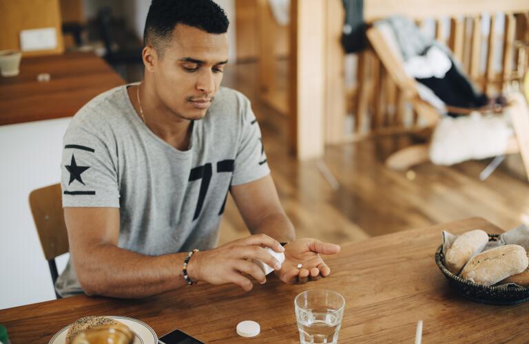Young Hispanic man taking pill at kitchen table