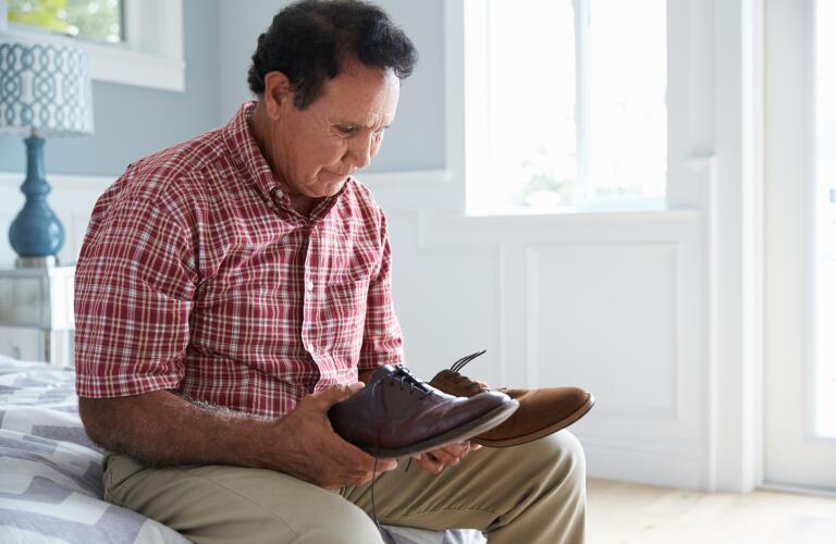Senior Caucasian man looking confused holding mismatched pair of shoes