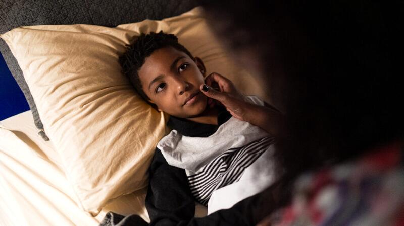 Mother caring for young son who is resting in bed
