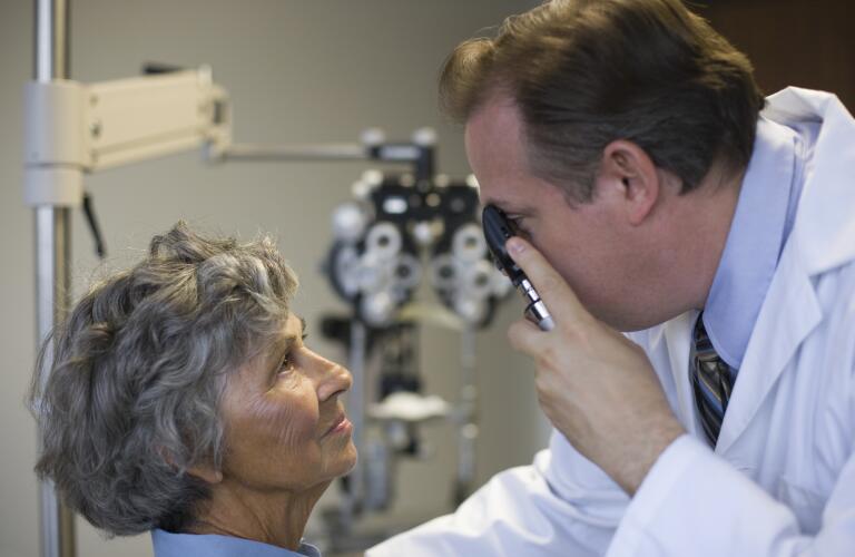 male Caucasian doctor examining senior female Caucasian's eyes