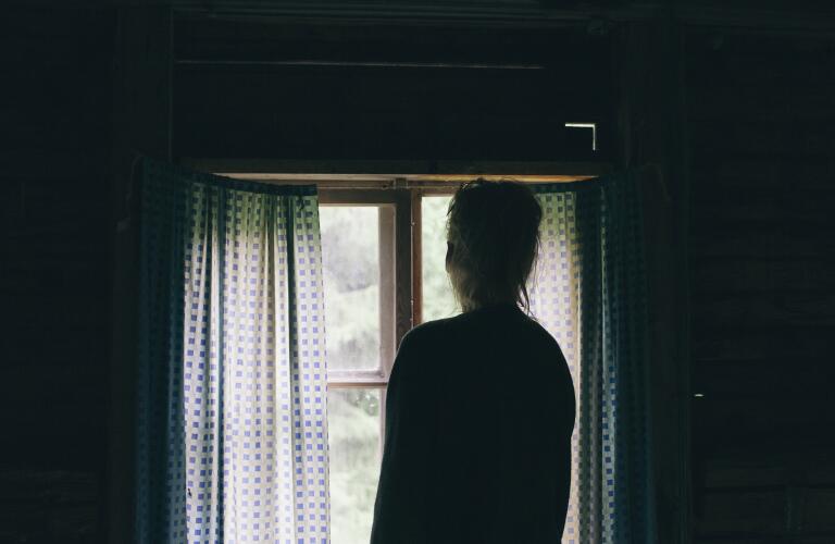 Rear view of woman in dark room looking through window at home