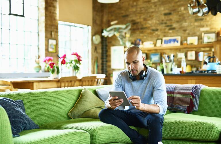 man using tablet while sitting on bright green couch in living area