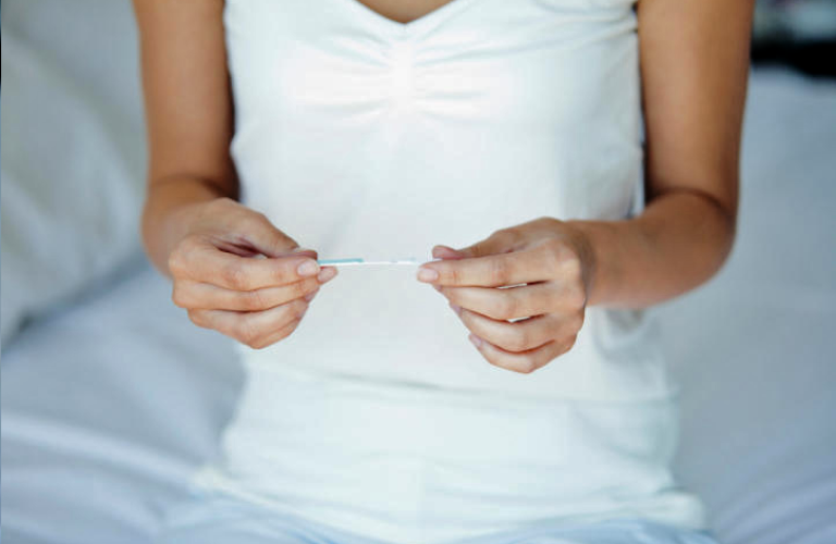Woman holding pregnancy test, mid section