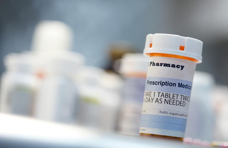 prescription medication bottle sitting on a countertop in front of other prescription medication bottles which are out of focus in the background