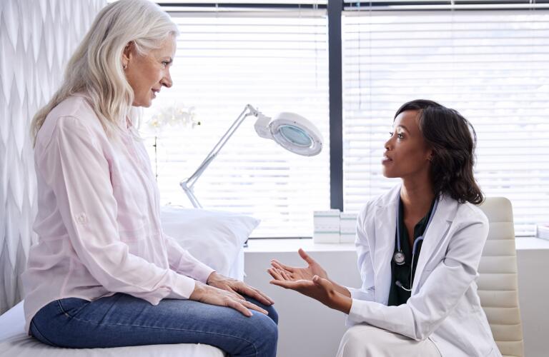 Young African American female dermatologist talking to older Caucasian female patient