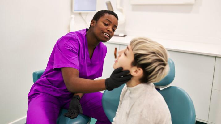 Dentist or dental hygienist examining mouth of young boy in dentist's office