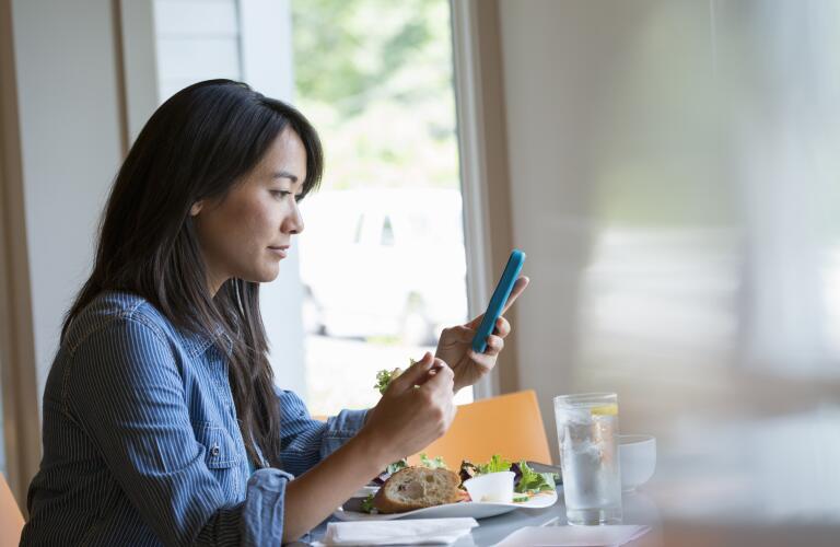 woman eating salad and checking phone