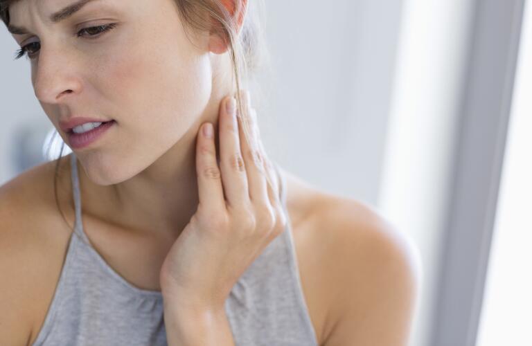 Young Caucasian woman touching side of neck and looking concerned