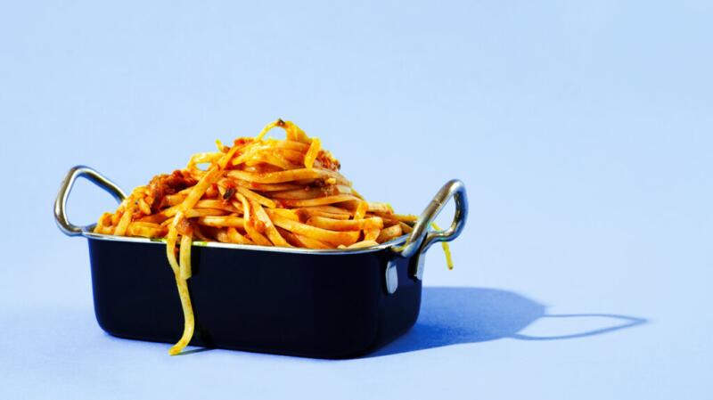 Spaghetti with red sauce in a casserole dish against a plain light blue background.