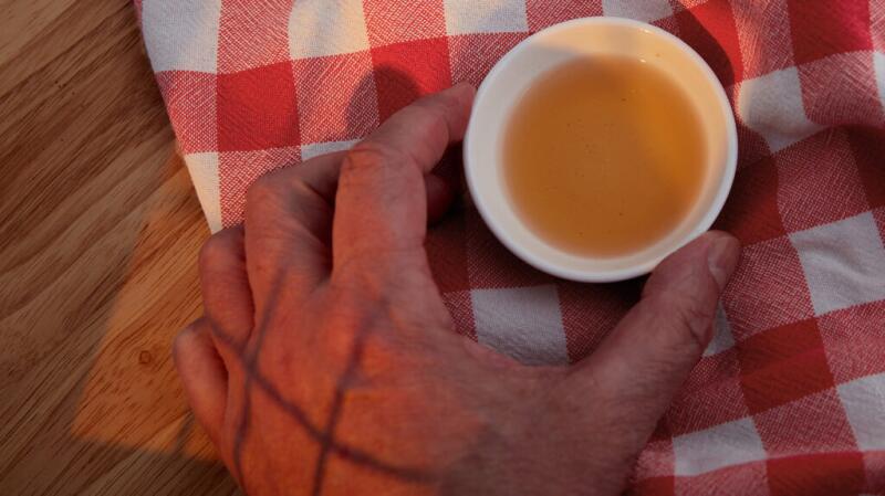 There is a closeup of a person holding a cup of apple cider vinegar.