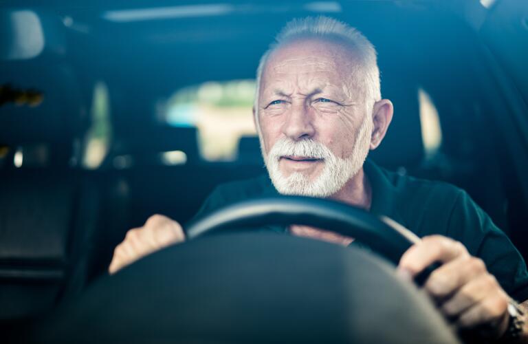 senior Caucasian male driving in car squinting with difficulty into distance