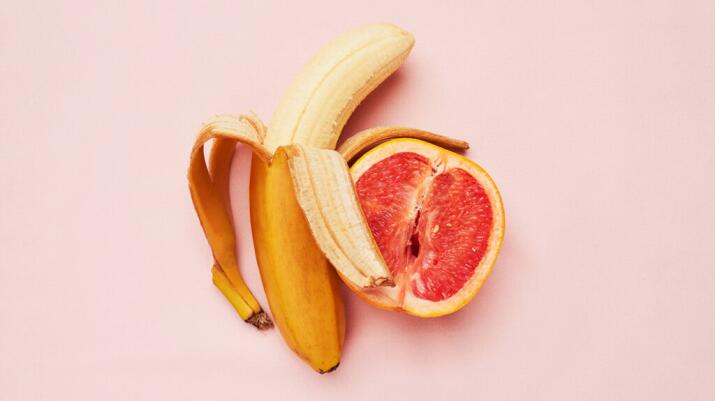 Un plátano y un pomelo sobre un fondo rosa.