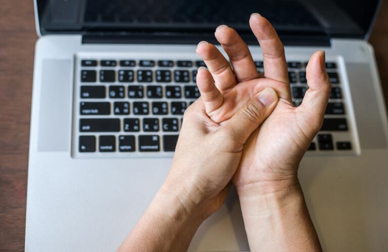 Cropped image of woman with hand pain over laptop