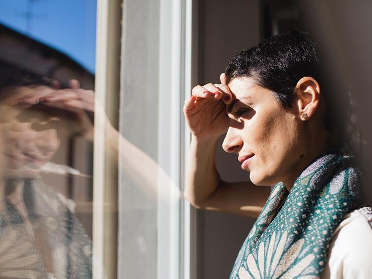 Woman standing by a window, shading her eyes from the sun