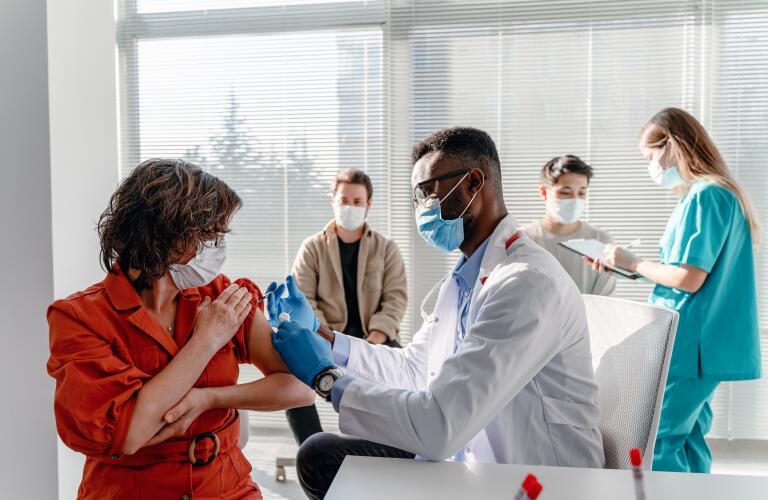 woman with face mask getting vaccinated for covid-19 at a clinic with other people waiting their turn