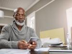 senior African American man holding smartphone in front of laptop