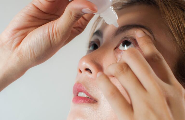 young woman applying medicine or saline drops in her eyes