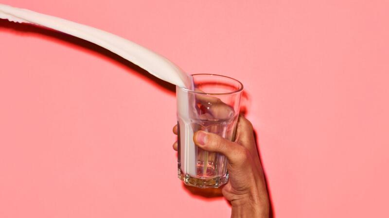 A closeup of a hand holding a glass of milk that is spilling