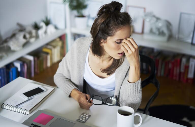 Young Caucasian woman at desk with headache or migraine or fatigue