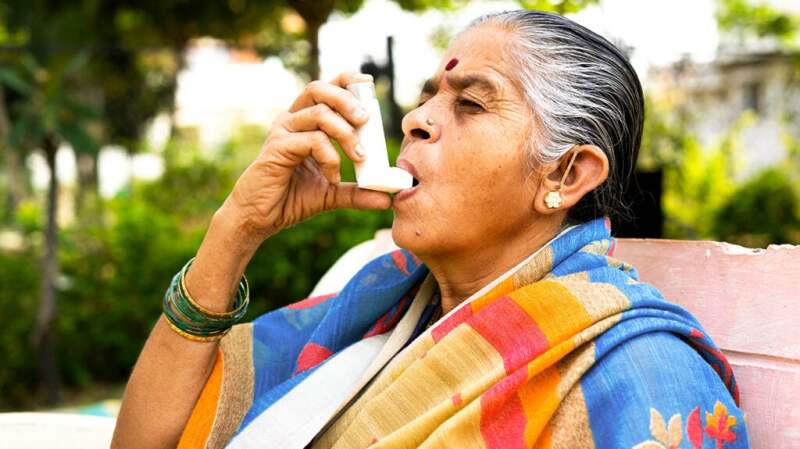 A woman sitting outdoors and using an inhaler