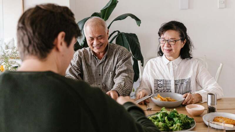 A family of two parents and an adult child sits together to eat.