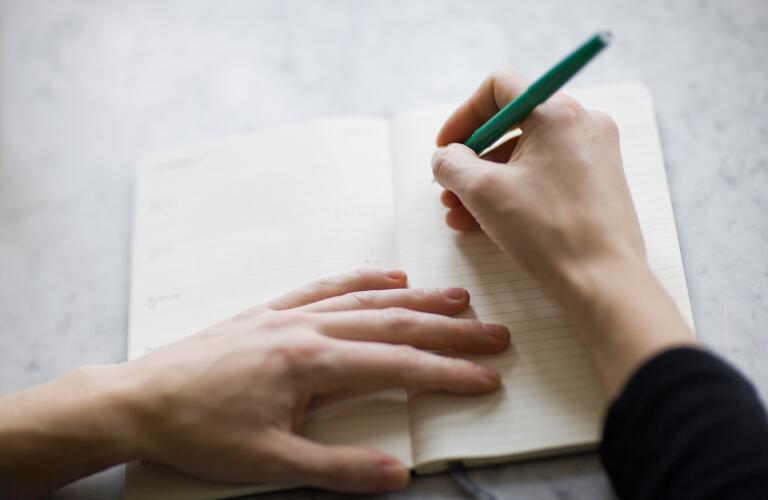 closeup of woman's hands making list in journal on table