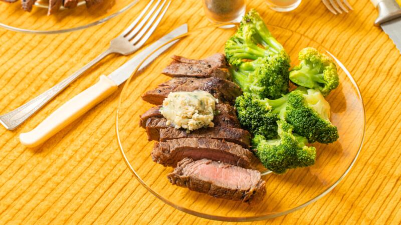 A plate of cut-up steak and broccoli sits on a wooden table.